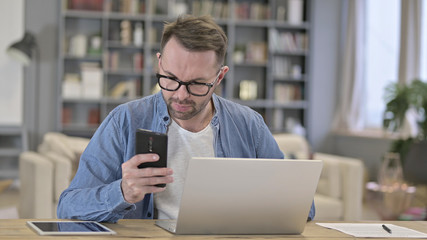 Focused Man using Smartphone and Working on Laptop
