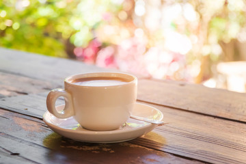 Coffee cup on wooden table in garden with bright bokeh nature background; copy space. 