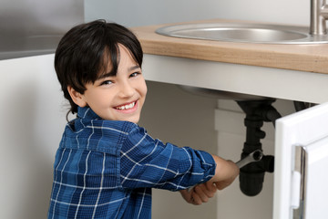Fototapeta na wymiar Little plumber repairing sink in kitchen