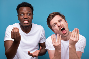 Two friends angry men looking angry showing italian gesture over blue background.