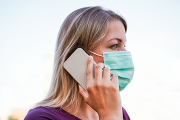 Young woman talking with mobile phone outdoor wearing face mask for Covid-19 virus prevention - Girl speaking with smartphone outside during quarantine isolation - Focus on finger