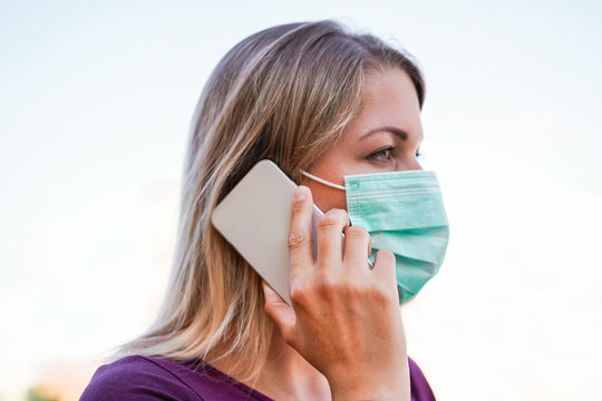 Young woman talking with mobile phone outdoor wearing face mask for Covid-19 virus prevention - Girl speaking with smartphone outside during quarantine isolation - Focus on finger - Powered by Adobe