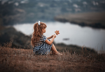 
long-haired girl sits on a cliff near the river in the summer