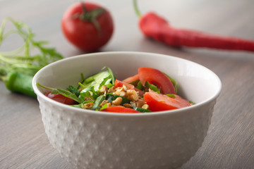 Healthy fresh summer salad with cucumbers, tomatoes, fresh arugula, chopped walnuts, pepper, olive oil and lemon juice on a rustic wooden surface