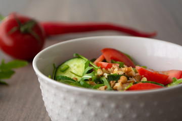 Healthy fresh summer salad with cucumbers, tomatoes, fresh arugula, chopped walnuts, pepper, olive oil and lemon juice on a rustic wooden surface