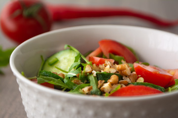 Healthy fresh summer salad with cucumbers, tomatoes, fresh arugula, chopped walnuts, pepper, olive oil and lemon juice on a rustic wooden surface
