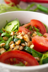 Healthy fresh summer salad with cucumbers, tomatoes, fresh arugula, chopped walnuts, pepper, olive oil and lemon juice on a rustic wooden surface