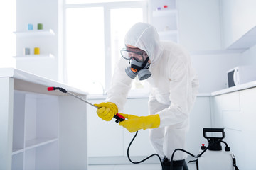 Profile side photo of focused cleaner coverall worker guy hold sprayer spray table shelves use protective equipment prevent covid spreading in kitchen house indoors
