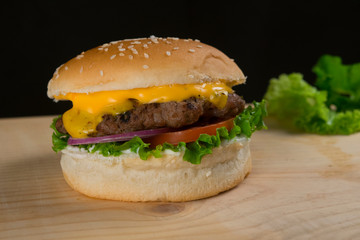 Delicious Beef Burger With Lettuce Tomato Onion Cheese on Wooden Table and Dark Background