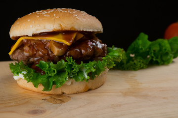 Delicious Grilled Hamburger With Lettuce Leaf on Wooden Table and Dark Background