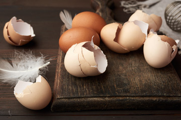brown raw chicken eggs, shells, cutting board and hand-held whisk for protein on a wooden table