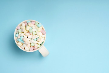 Mixed colored mini marshmallow sweets in white mug on blue background