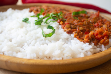 Red lentil ragu dahl with tomatoes, pepper, greens and rice on a wooden plate