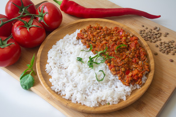 Red lentil ragu dahl with tomatoes, pepper, greens and rice on a wooden plate