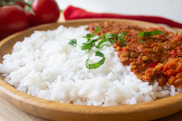 Red lentil ragu dahl with tomatoes, pepper, greens and rice on a wooden plate