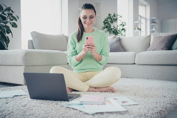 Portrait of her she nice attractive lovely pretty focused cheerful girl sitting on floor working remotely typing sms chatting preparing finance plan at light white interior house living-room