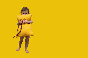 a beautiful little girl with a yellow pillow, looking at the camera laughing and hugging a pillow on a yellow background, Concept of comfortable pillows for everyone
