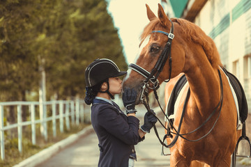 Young teenage girl equestrian kissing her favorite red horse. Multicolored outdoors horizontal...