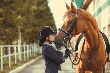 Young teenage girl equestrian kissing her favorite red horse. Multicolored outdoors horizontal...