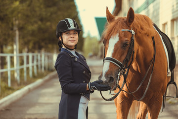 Beautiful professional female jockey standing near horse. woman horse rider is preparing to...
