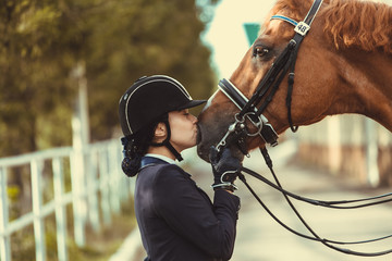 Young teenage girl equestrian kissing her favorite red horse. Multicolored outdoors horizontal image. Dressage outfit  - 344500982