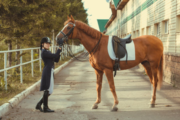Beautiful professional female jockey standing near horse. woman horse rider is preparing to...