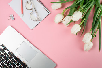 Business woman concept. Laptop white tulips and glasses on a pink background.