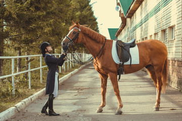horsewoman jockey in uniform standing with black horse outdoors
