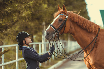 horsewoman jockey in uniform standing with black horse outdoors