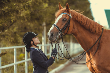 horsewoman jockey in uniform standing with black horse outdoors