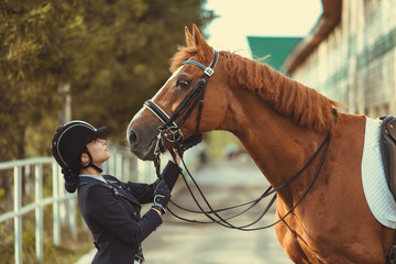 horsewoman jockey in uniform standing with black horse outdoors