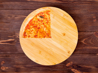 Quarter of pizza with mozzarella, bocconcini and basil leaves or pizza margherita on round wood plate which is on wooden rustic background, top view