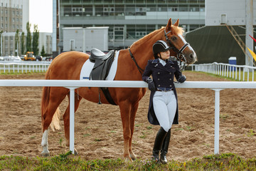 Beautiful professional female jockey standing near horse. woman horse rider is preparing to...