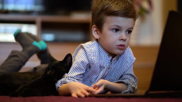 Funny child with kitten using a laptop at home