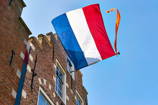 Dutch flag with orange streamer waving in the wind on the facade of a typical dutch house with stepped gable on Koningsdag. A national holiday in the Kingdom of the Netherlands.   