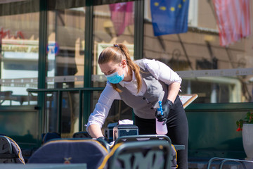 Waitress with a mask disinfects the table of an outdoor bar, café or restaurant, reopen after...