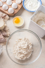 Baking background with flour in bowl, eggs and ingredients on white kitchen table background, top view. Home Bake. Recipes to cookies, pie and cake