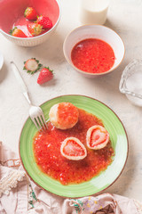 Close up of tasty boiled cottage dumplings stuffed  with fresh strawberries with sweet berries sauce on white kitchen table. Top view. Summer sweet food. Home cooking. Seasonal meal. Knedliki .