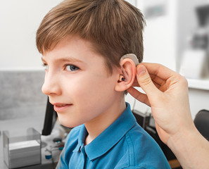 Installation hearing aid on сaucasian boy's ear. Hearing treatment at clinic