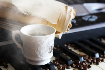 A clock with Roman numerals and a piano, coffee beans and a white cup and steam