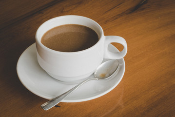 A cup of hot coffee with spoon and coasters for coffee isolated on wooden table, horizontal view.
