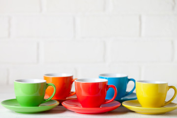 Colorful cups on the white background of a brick wall. Background with copy space. Horizontal. Selective focus.