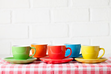 Colorful cups on the white background of a brick wall. Background with copy space. Horizontal. Selective focus.
