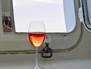 Glas of Rose wine and porthole window of oceanview stateroom or cabin on classic cruiseship or...