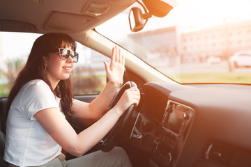 Woman in sunglasses driving car in a sunny day and saluting familiar driver or a pedestrian.