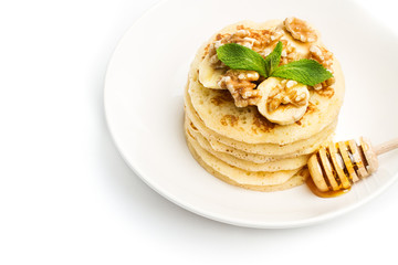 Tortitas con rodajas de plátanocon nueces y menta sobre un plato blanco redondo con batuta con miel sobre un fondo blanco aislado. Vista superior. Copy space