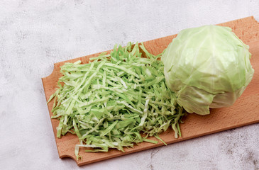 Young cabbage head and shredded cabbage on a wooden cutting board on a light gray background. Top...