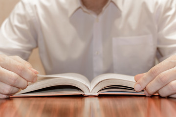 man reading open book on table close up