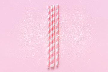 Pastel paper straws with white stripes on soft pink background with sparkles. Festive concept. Flat...