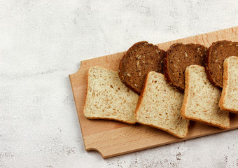 Slices of multigrain bread and rye bread on a wooden cutting board on a light gray background. Top view, flat lay